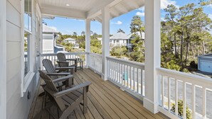 A covered porch with wooden chairs and a ceiling fan, overlooking a residential area with houses and trees. - 30A Salt Life by Avantstay Golf Cart + Pool Blue Mountain (Santa Rosa Beach)
