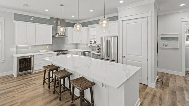 A modern kitchen with white cabinetry, a large island with bar stools, stainless steel appliances, and pendant lighting. - 30A Salt Life by Avantstay Golf Cart + Pool Blue Mountain (Santa Rosa Beach)