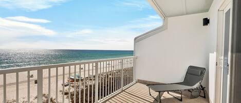 A balcony with a view of the beach and ocean, a chair, and a door.
