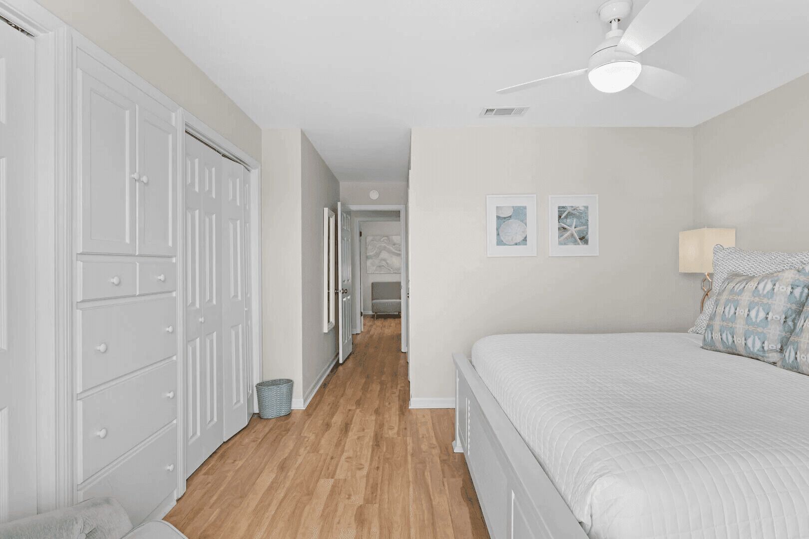 Une chambre à coucher avec un lit, un ventilateur de plafond et un couloir menant à une autre pièce.