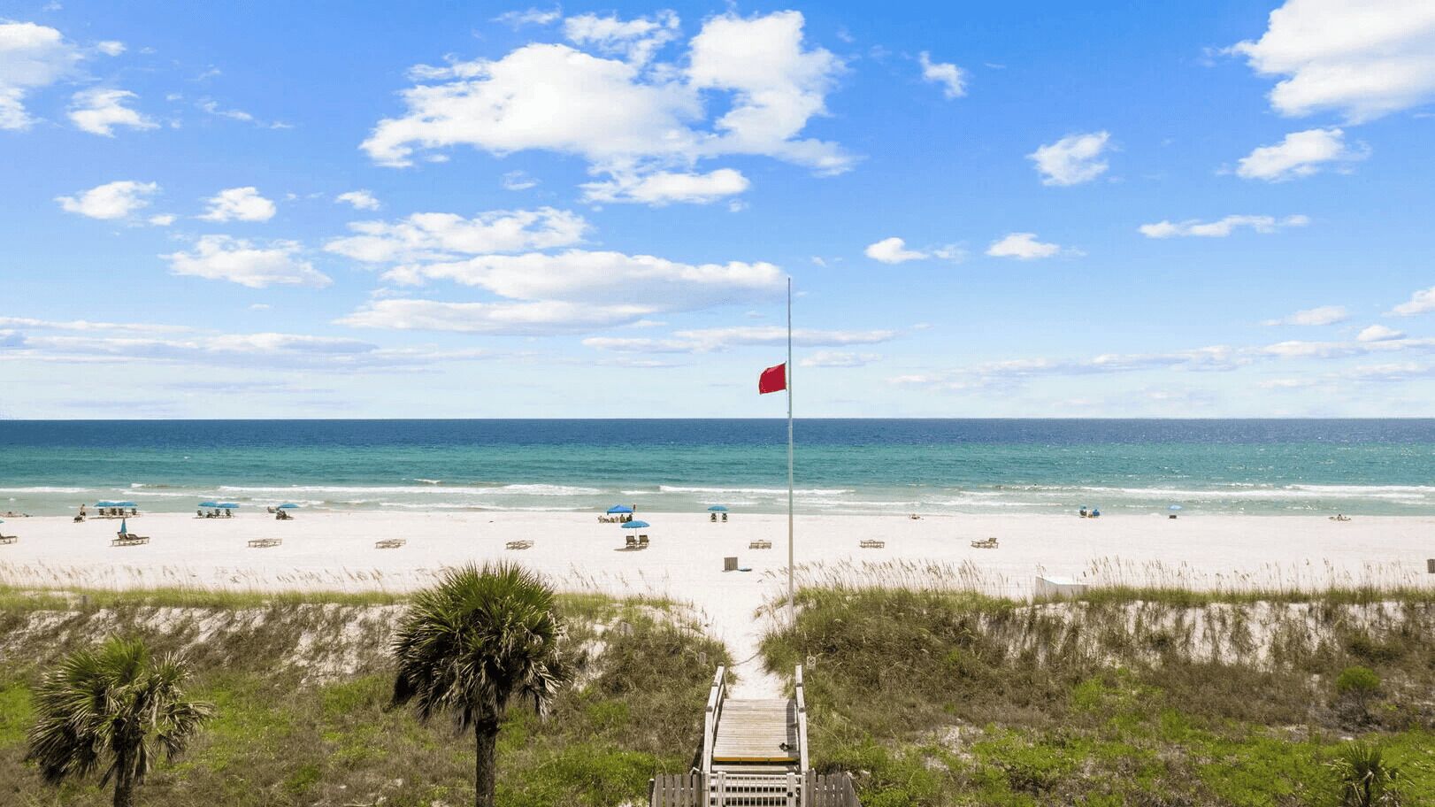 A beach with a flag, sand, and ocean.