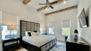 A bedroom with a large bed, a ceiling fan, and a view of the outdoors through the windows.
