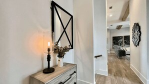 A modern interior with a wooden console table, a wall-mounted geometric mirror, and a decorative vase with dried flowers.