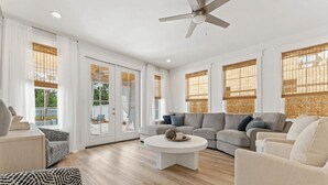 Un salon spacieux avec un grand canapé d’angle, une table basse ronde et un ventilateur de plafond.