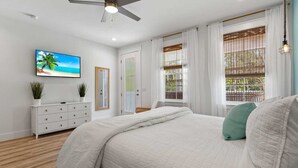 Une chambre à coucher avec un lit, une commode, un téléviseur et une fenêtre avec des rideaux.