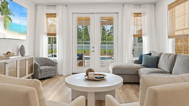Un salon moderne avec une table basse ronde, deux canapés, un meuble et une grande fenêtre donnant sur une piscine et un espace verdoyant.