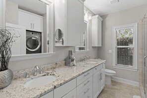 A modern bathroom with a double sink vanity, a built-in washing machine, and a window with blinds. - Honey Bee Bungalows by Avantstay Boat Friendly, Pool Access (Miramar Beach)