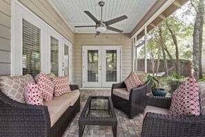 A covered porch with wicker furniture, a ceiling fan, and a view of trees. - Honey Bee Bungalows by Avantstay Boat Friendly, Pool Access (Miramar Beach)