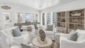 A spacious living room with a pool table, white furniture, and a large wooden bookshelf.