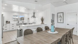A modern kitchen with white cabinetry, a wooden dining table, and wicker chairs.