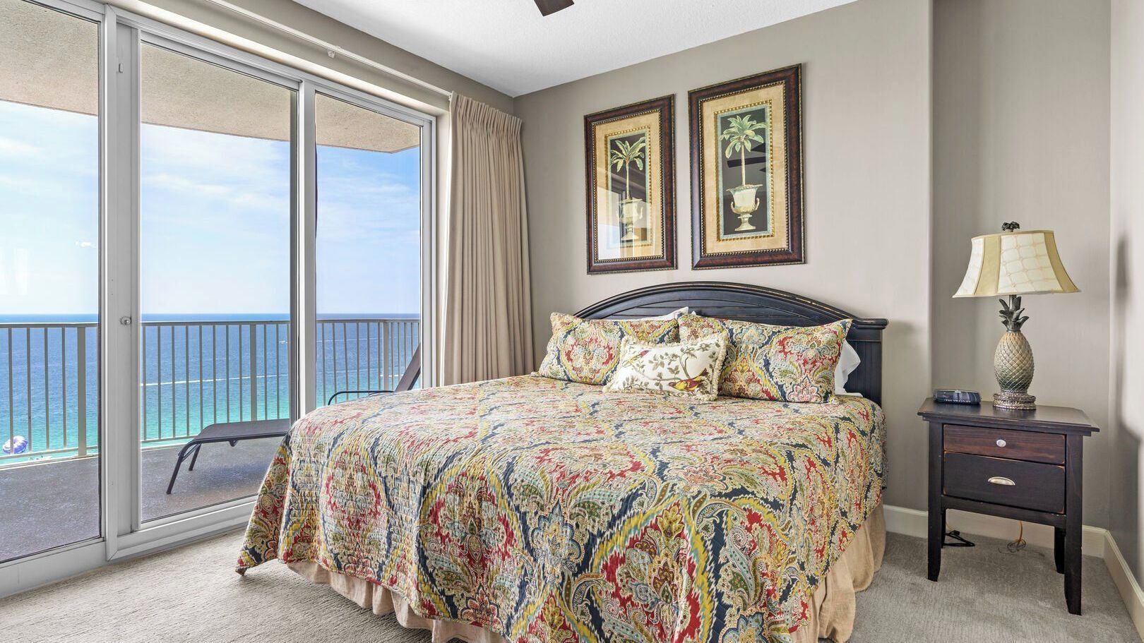 A bedroom with a bed, a nightstand, a lamp, and a view of the ocean through a sliding door.