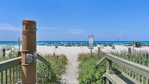 A beach pathway leading to the ocean with a wooden fence, a metal pole, and a beach sign.