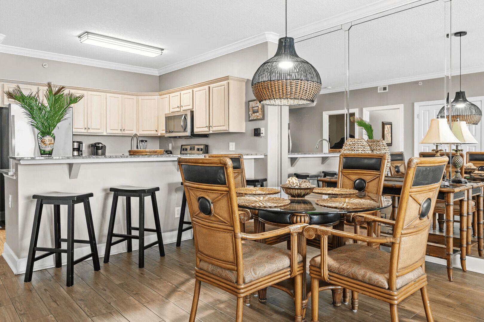 A modern kitchen with a central island, bar stools, wicker chairs, and a dining table.