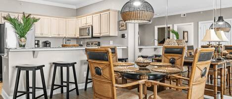 A modern kitchen with a central island, bar stools, wicker chairs, and a dining table.