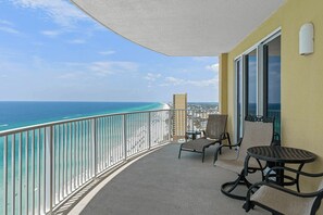 A balcony with a view of the ocean, a chair, a small table, and a window.