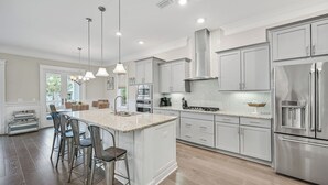 Una cocina moderna con armarios blancos, electrodomésticos de acero inoxidable e iluminación colgante.