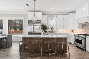 Una cocina moderna con armarios blancos, electrodomésticos de acero inoxidable y una isla central con taburetes de bar.