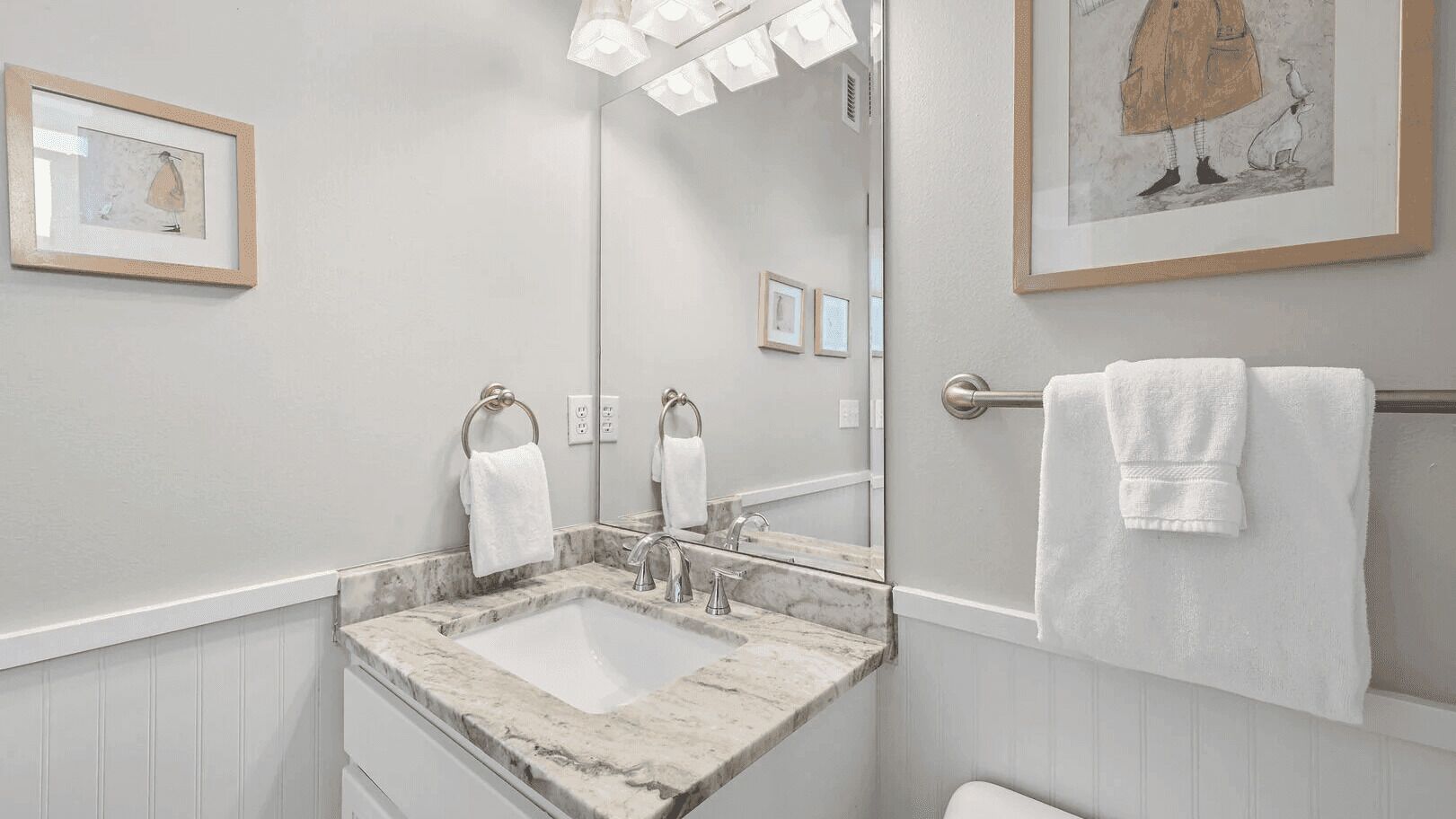 Un bagno con un lavandino in marmo, due anelli per asciugamani, un grande specchio e opere d'arte incorniciate alle pareti.