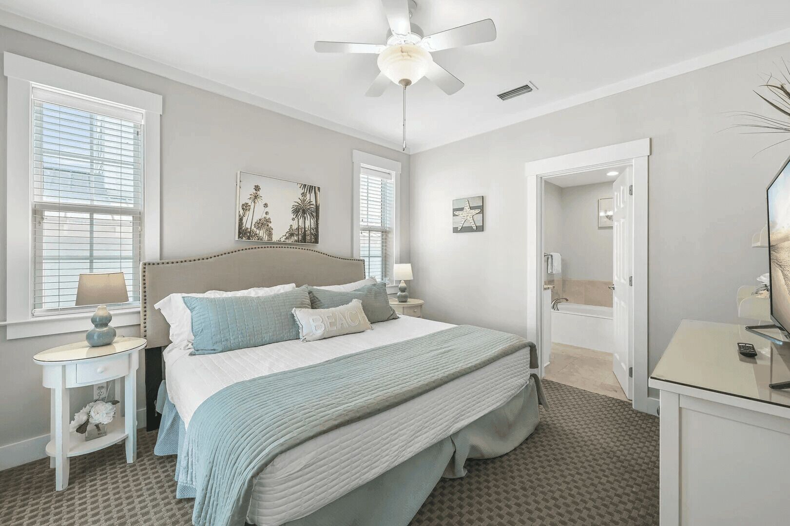 A bedroom with a bed, bedside tables, a ceiling fan, and artwork on the walls.
