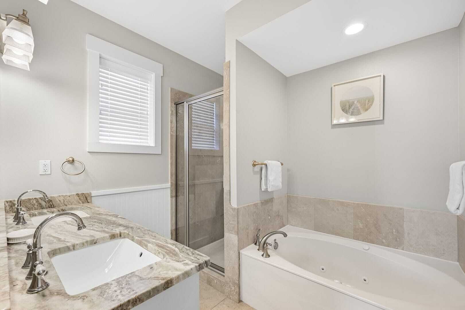 Une salle de bain avec un lavabo en marbre, une baignoire, une douche et une fenêtre avec des stores.