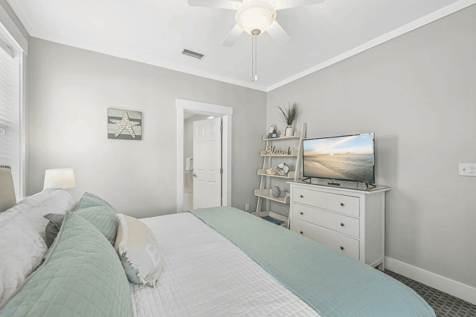 A bedroom with a bed, a TV on a dresser, a ceiling fan, and a door.