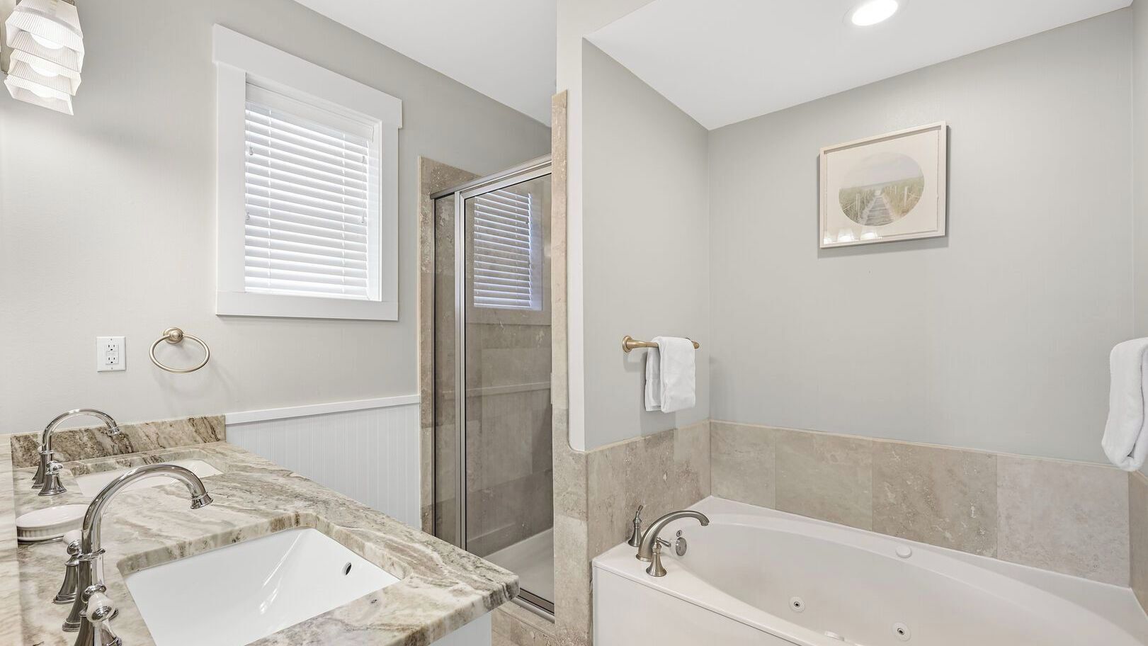 Une salle de bain avec deux éviers, une baignoire, une douche et un tableau encadré au mur.
