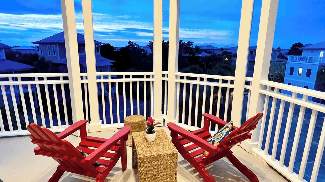 A balcony with white railings, two red chairs, a small table, and a potted plant.