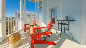 Un porche abrité avec deux fauteuils Adirondack rouges, un panier en osier et une petite table sur laquelle est posée une plante.
