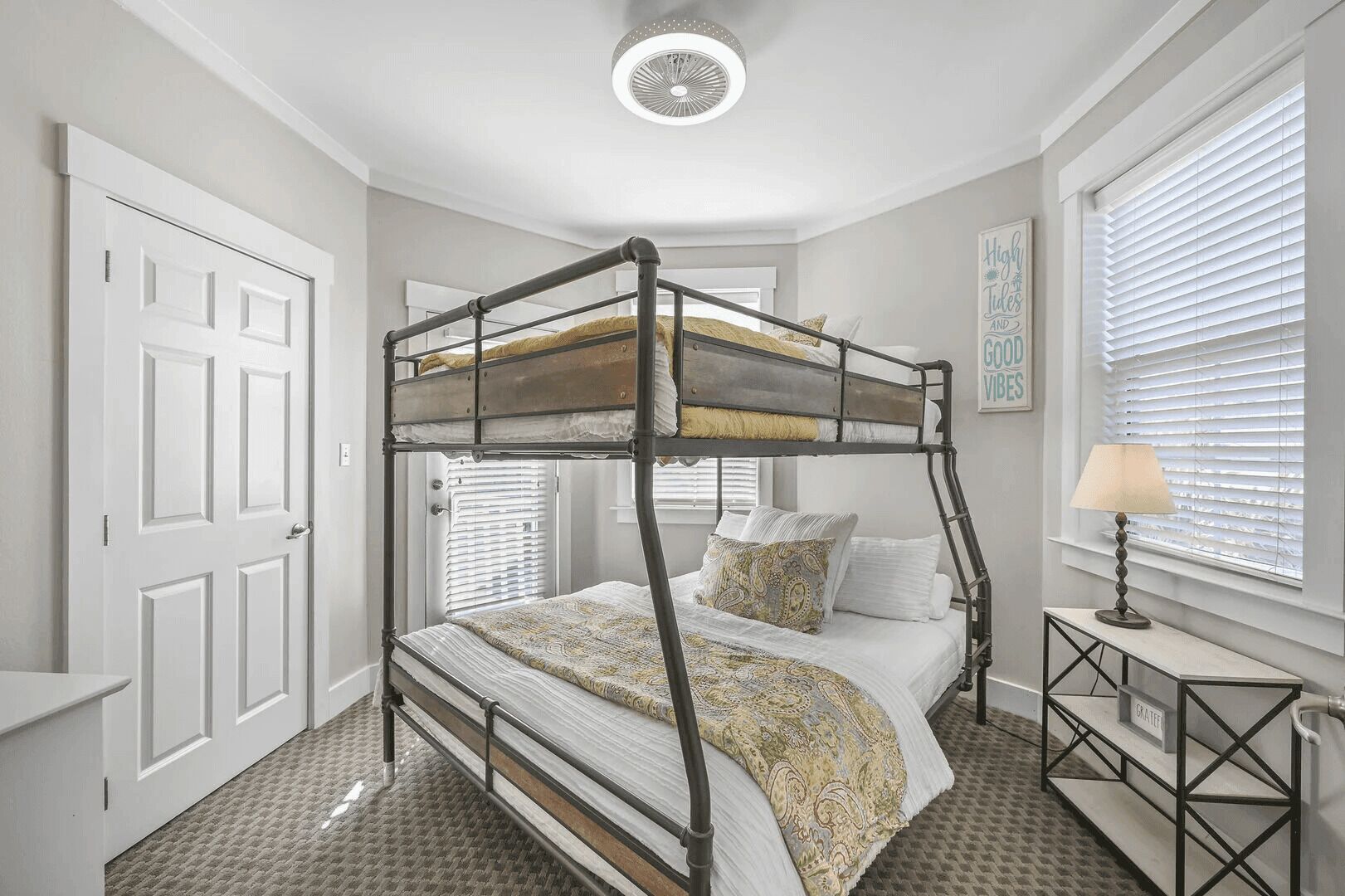 A bunk bed room with a desk and lamp, white walls, and a ceiling fan.