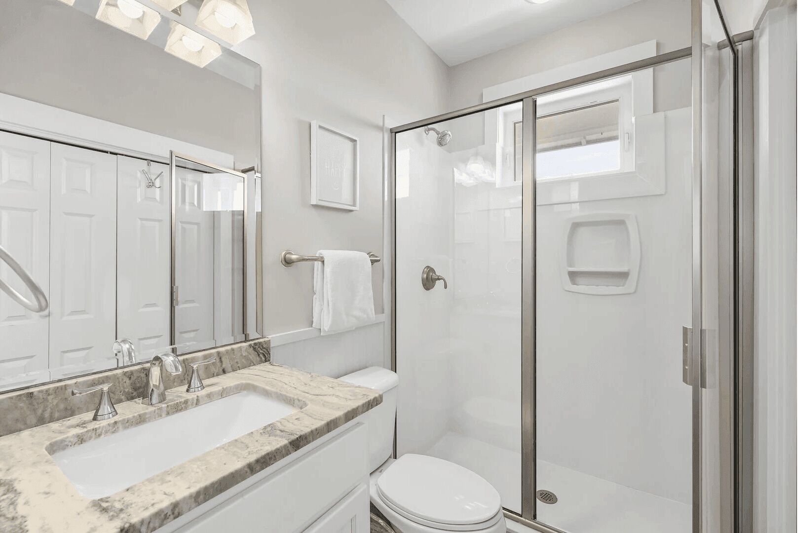 Un baño moderno con ducha de vidrio, un espejo grande y un lavamanos de mármol.