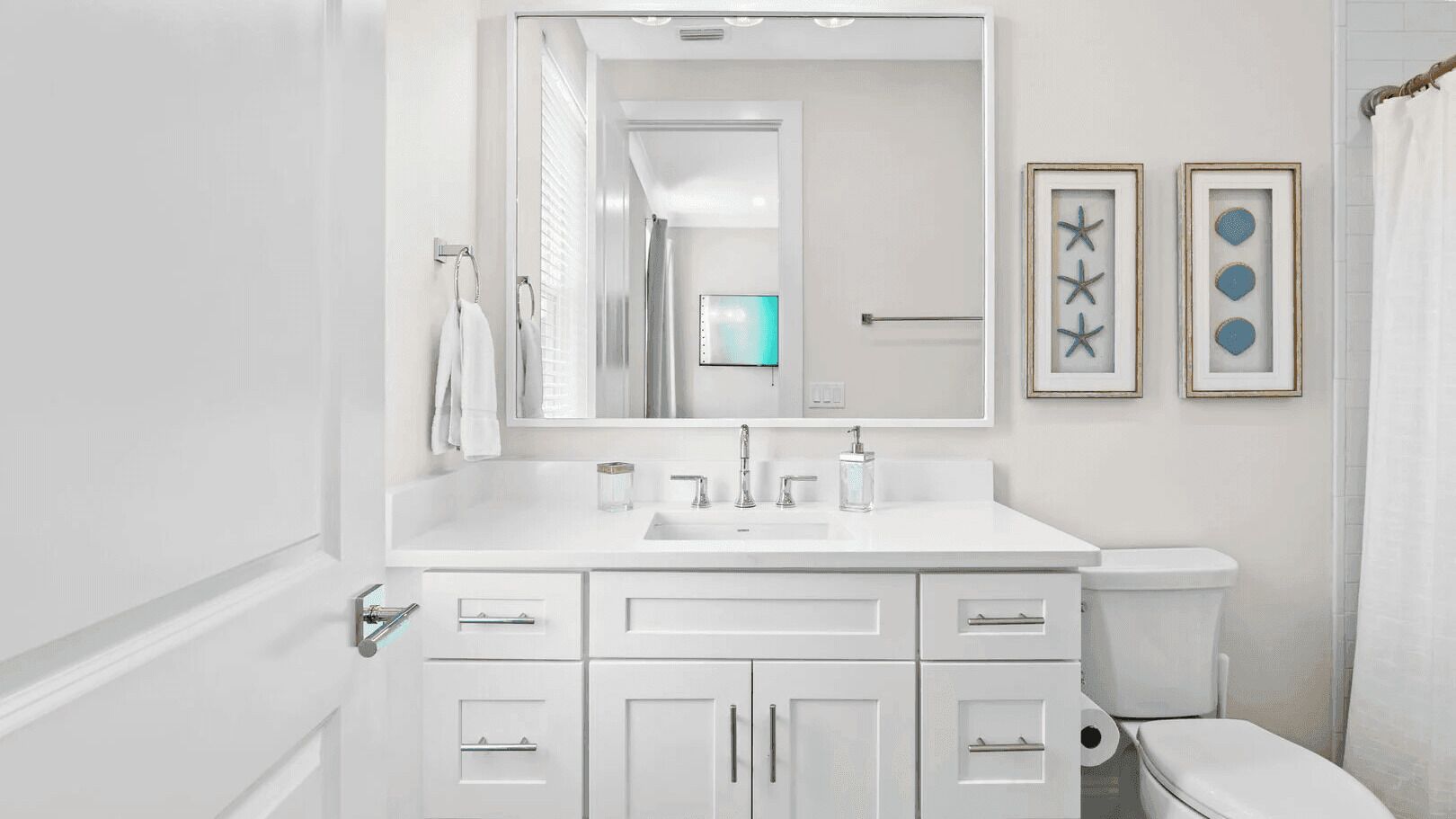 Une salle de bain avec un meuble-lavabo blanc, un grand miroir, des toilettes et des œuvres d’art encadrées accrochées au mur.