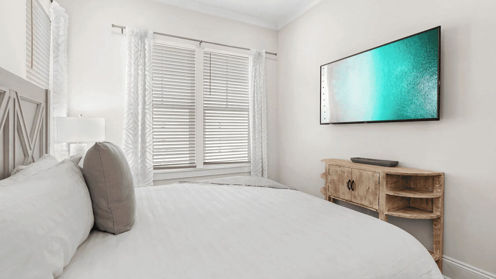 Une chambre à coucher avec un lit, une table de chevet en bois, une télévision et une fenêtre avec des stores.