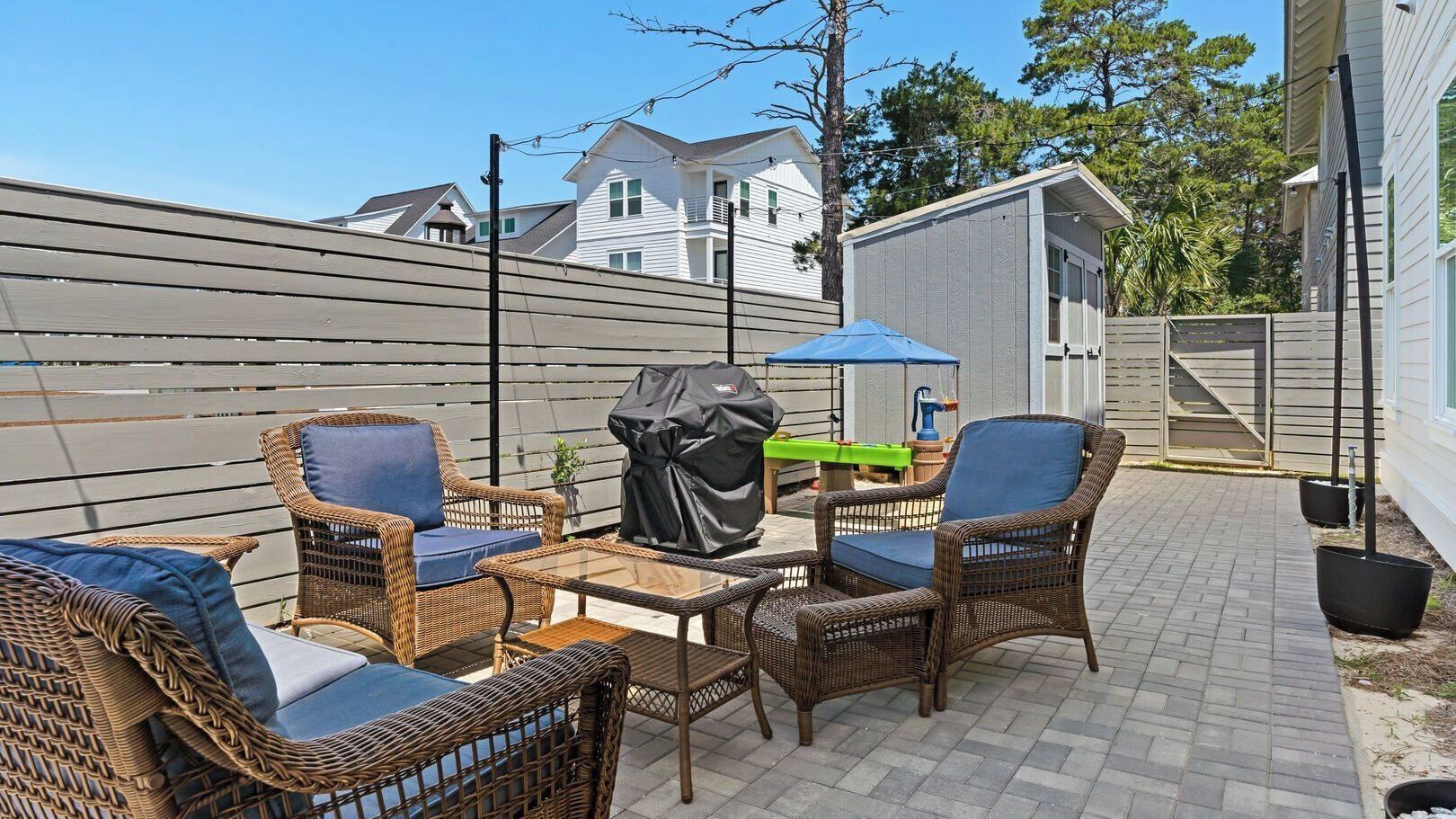 Une terrasse avec des meubles en osier, un barbecue et un petit abri de jardin.