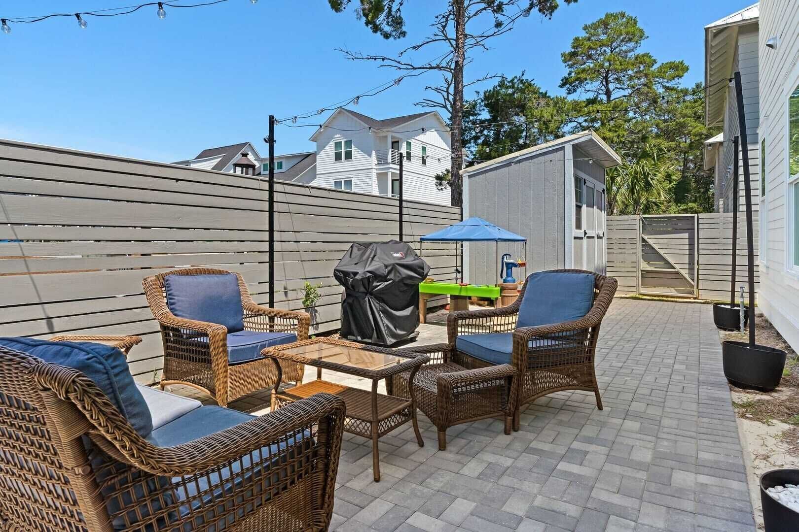 An outdoor patio with wicker furniture, a grill, and a blue umbrella.