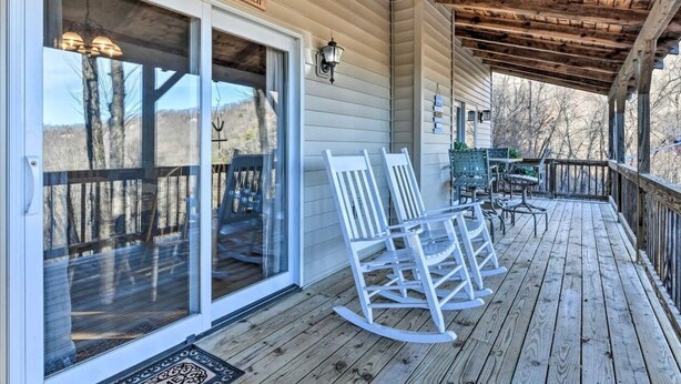Eine hölzerne Veranda mit Schaukelstühlen, einem Willkommensschild und einer Glasdoor zu einer Terrasse.