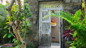 Un edificio rústico de piedra con una puerta de madera, rodeado de exuberante vegetación tropical y una pequeña piscina.