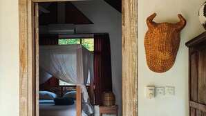 Un umbral que da a un dormitorio con una cama, una cesta tejida en la pared y una escultura tradicional de madera.