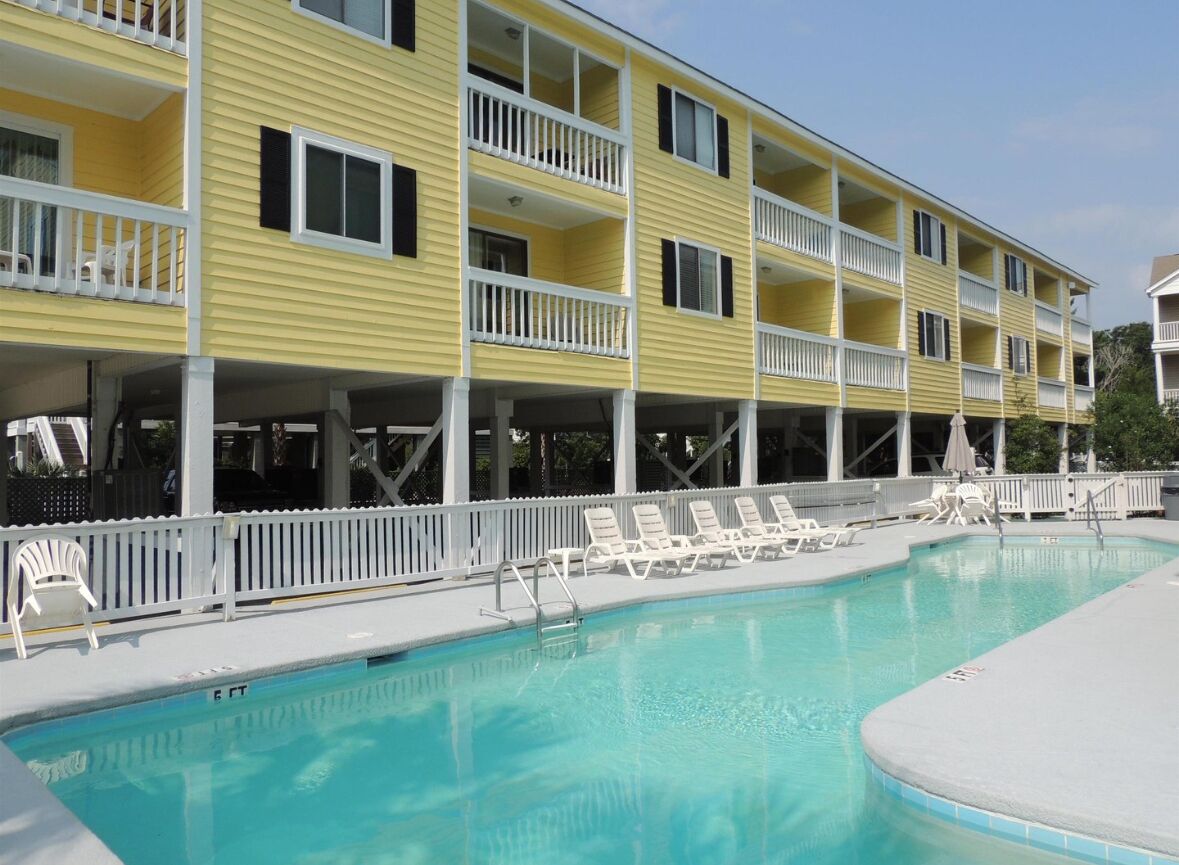 Un edificio amarillo con balcones y una piscina con sillas de descanso.
