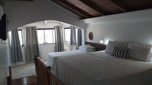 A bedroom with a large bed, a wooden headboard, a small bedside table, and a window with curtains. - Czaritza Apart Hotel (Bombinhas)