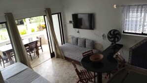 A room with a bed, a TV, a dining table, and a view of the outside. - Czaritza Apart Hotel (Bombinhas)