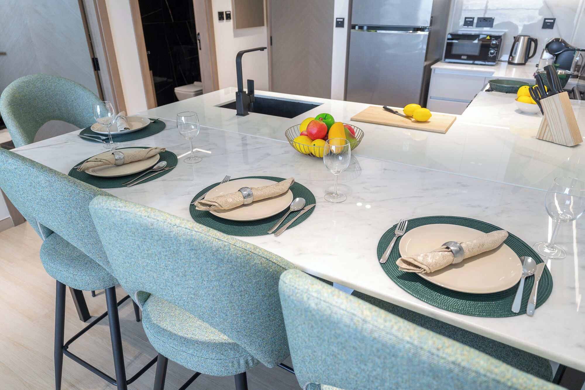Une table à manger dressée avec des assiettes, des couverts et un saladier rempli de fruits.
