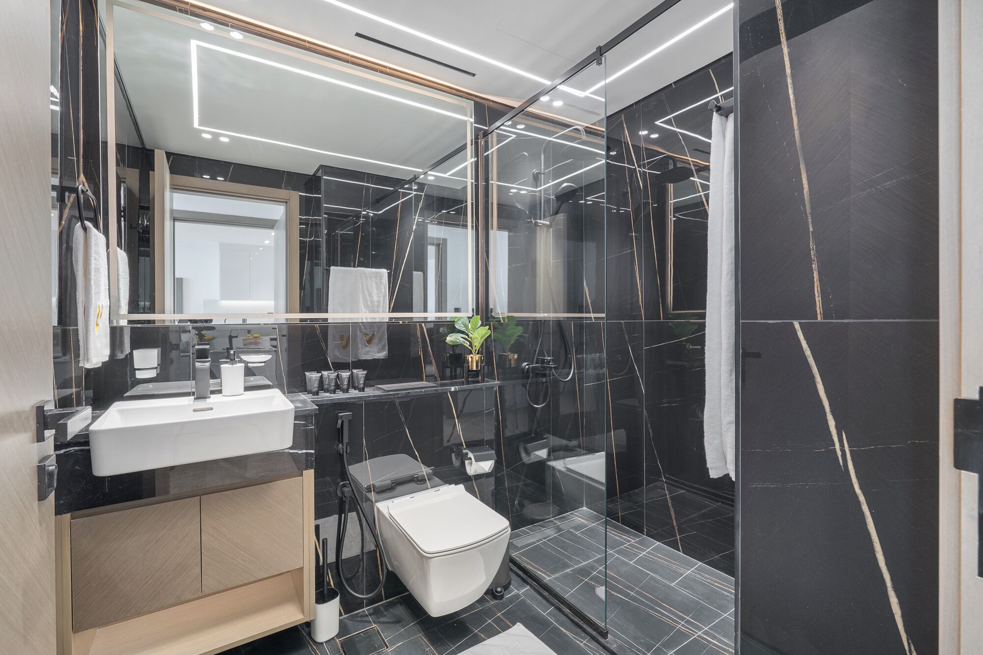 Une salle de bain moderne avec un grand miroir, un lavabo blanc, des toilettes et un espace douche.