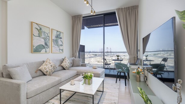 A modern living room with a grey sofa, a coffee table, and a large TV screen. - Vogue 7 mins Sky Dubai 3 mins Cirle Mall (Dubai)