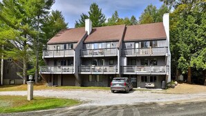 A two-story building with balconies, a car parked in front, and a dirt road leading to it. - Killington condo 5 min to killington resort (Killington)