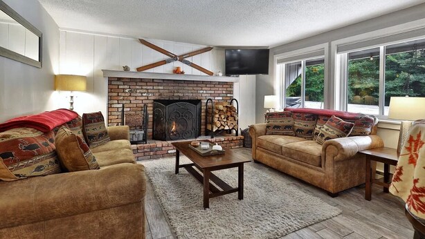 A cozy living room with a brick fireplace, two sofas, a coffee table, and a TV mounted on the wall. - Killington condo 5 min to killington resort (Killington)