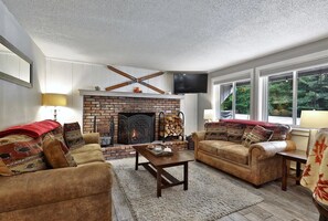 Ein gemütliches Wohnzimmer mit Kamin, zwei Sofas, einem Couchtisch und einem an der Wand befestigten Fernseher.