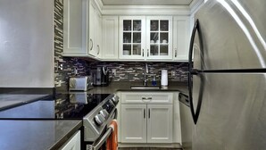 A modern kitchen with white cabinets, a stainless steel refrigerator, a black stovetop, and a tiled backsplash. - Killington condo 5 min to killington resort (Killington)
