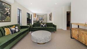 A modern living room with a green sofa, a round ottoman, and a wooden cabinet.