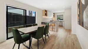 A modern kitchen with a central island, a dining area with a wooden table and green chairs, and a large sliding glass door leading to an outdoor area.