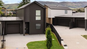 A modern two-story house with a garage, a small front yard, and a view of distant hills.